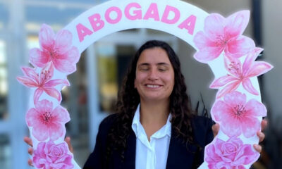 La foto muestra a Pia Ricchieri sosteniendo un cartel con su nombre y que dice abogada. Ella sonríe y el cartel tiene flores rosadas.